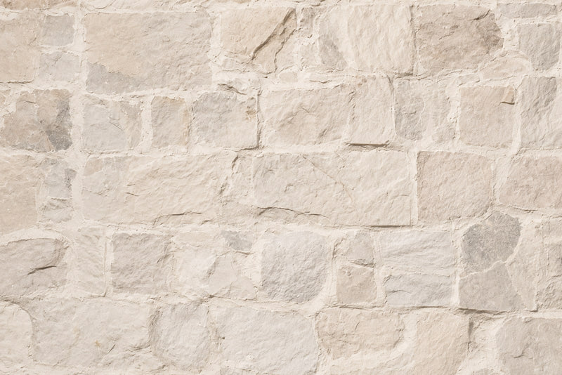 A cream limestone wall laid in rough cut blocks with wide pale mortar joints.