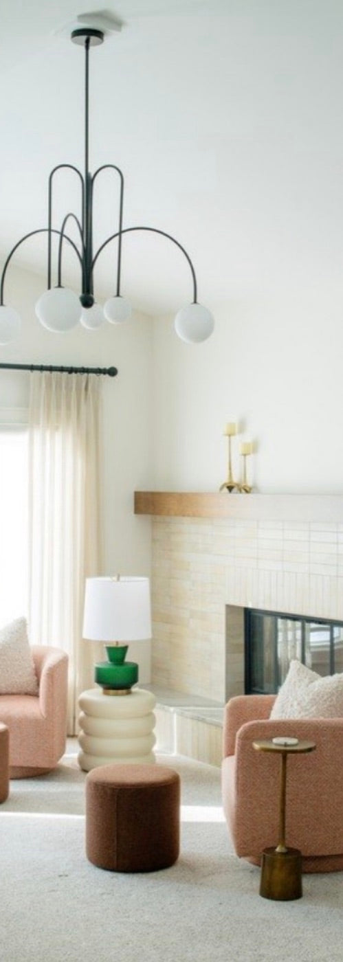 A sitting area with blush chairs, a green lamp and a black arched pendant