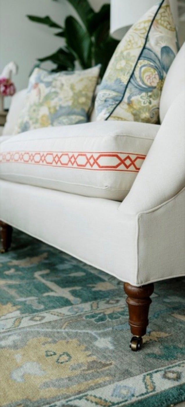 A white skirted sofa with patterned pillows on a blue and gold rug