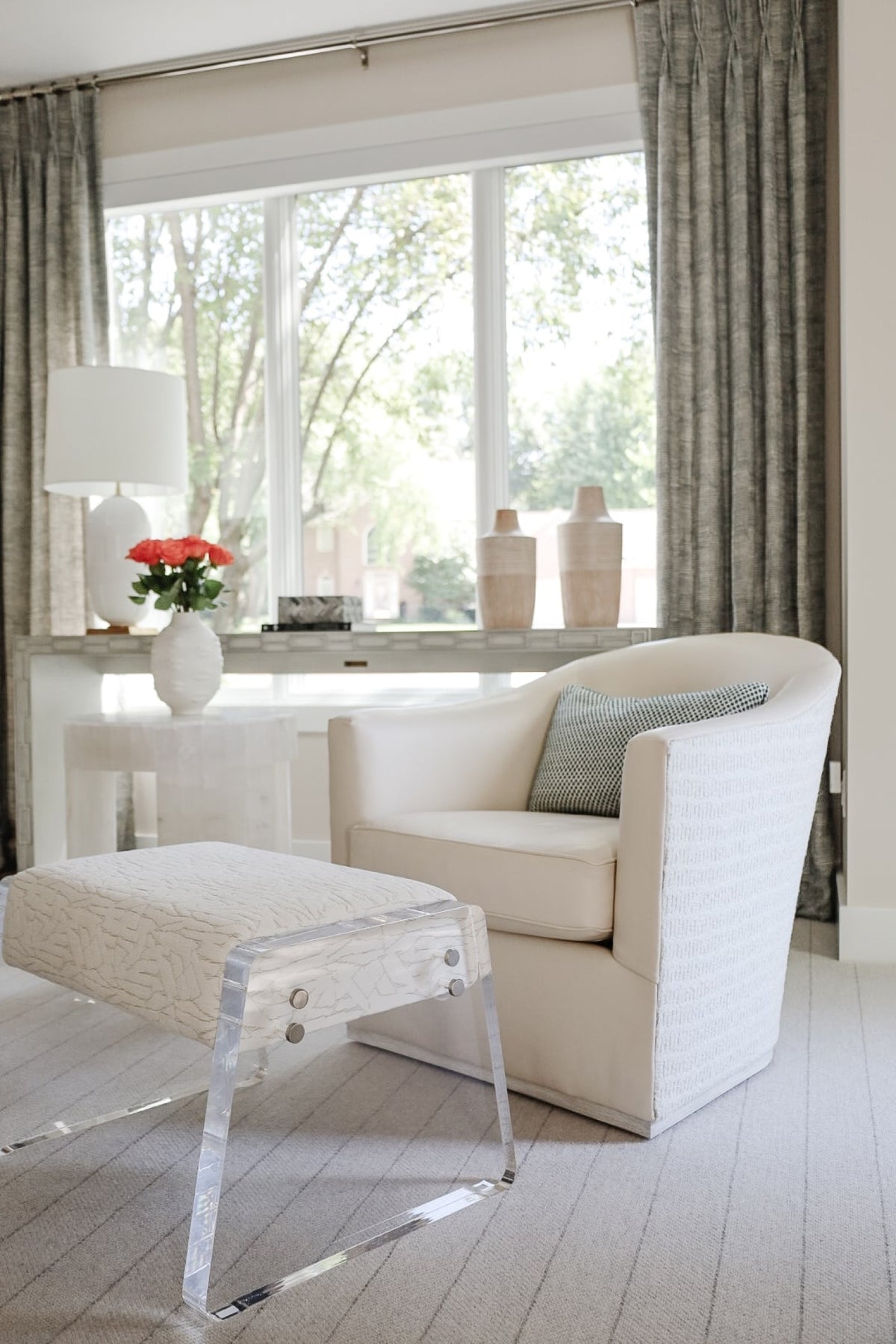A cream living room in Clive with a curved swivel chair and a lucite bench by the window.