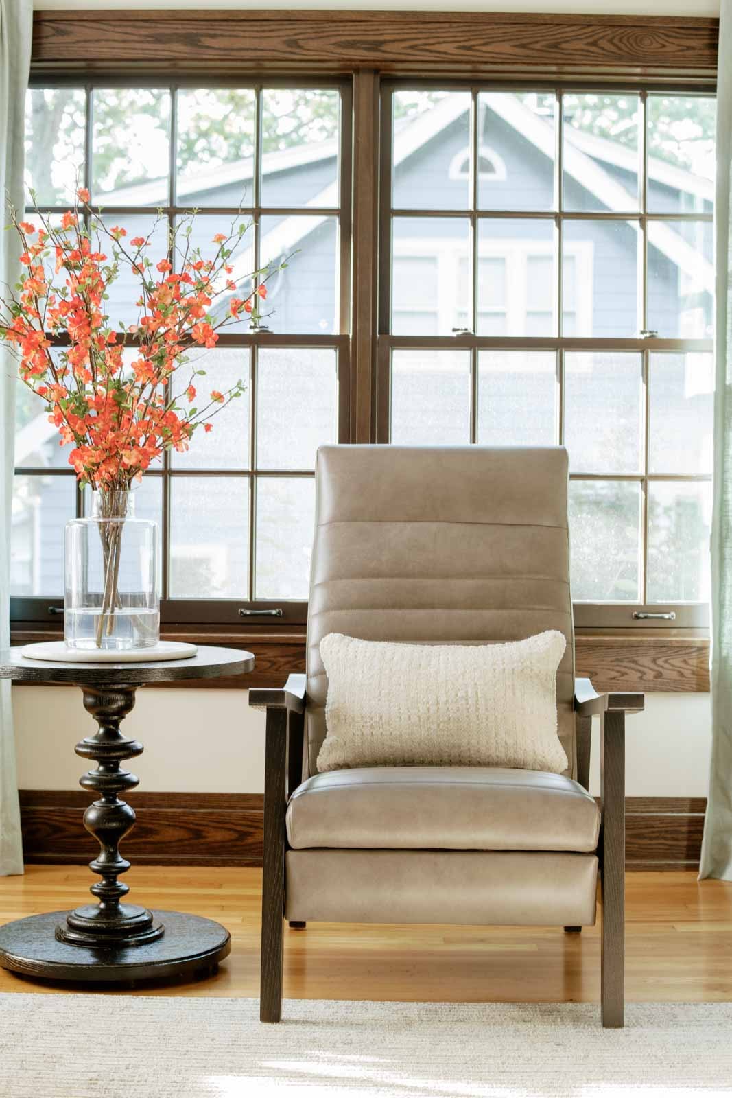 A living room in Des Moines with a taupe leather armchair on a dark wood frame beside a tall window.