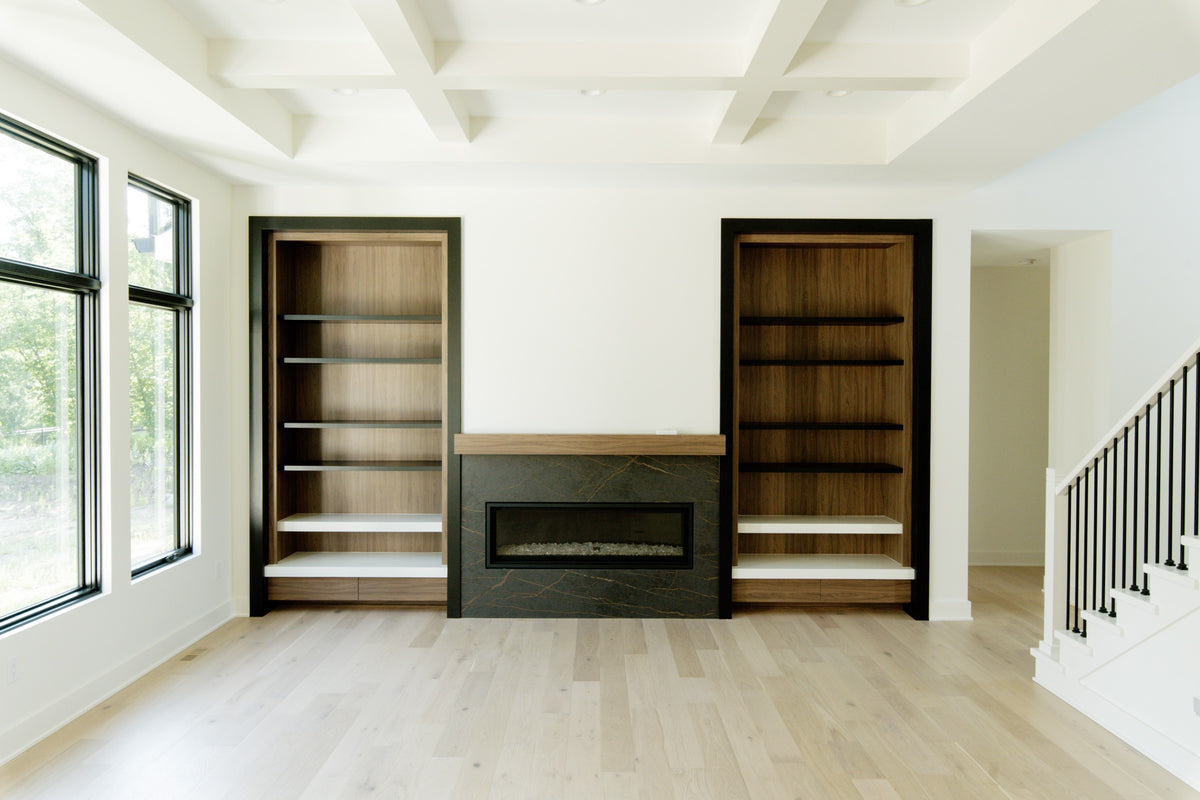 A living room in Waukee with a black framed walnut built-in beside a dark stone fireplace, over pale white oak floors.