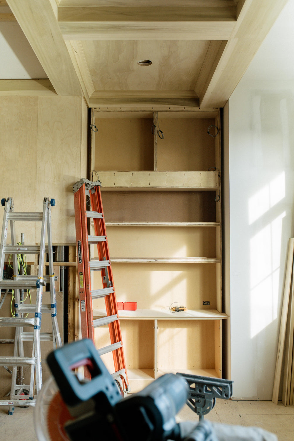 A floor to ceiling built-in cabinet going in under construction in Urbandale, with raw maple shelves and a coffered wood ceiling above.