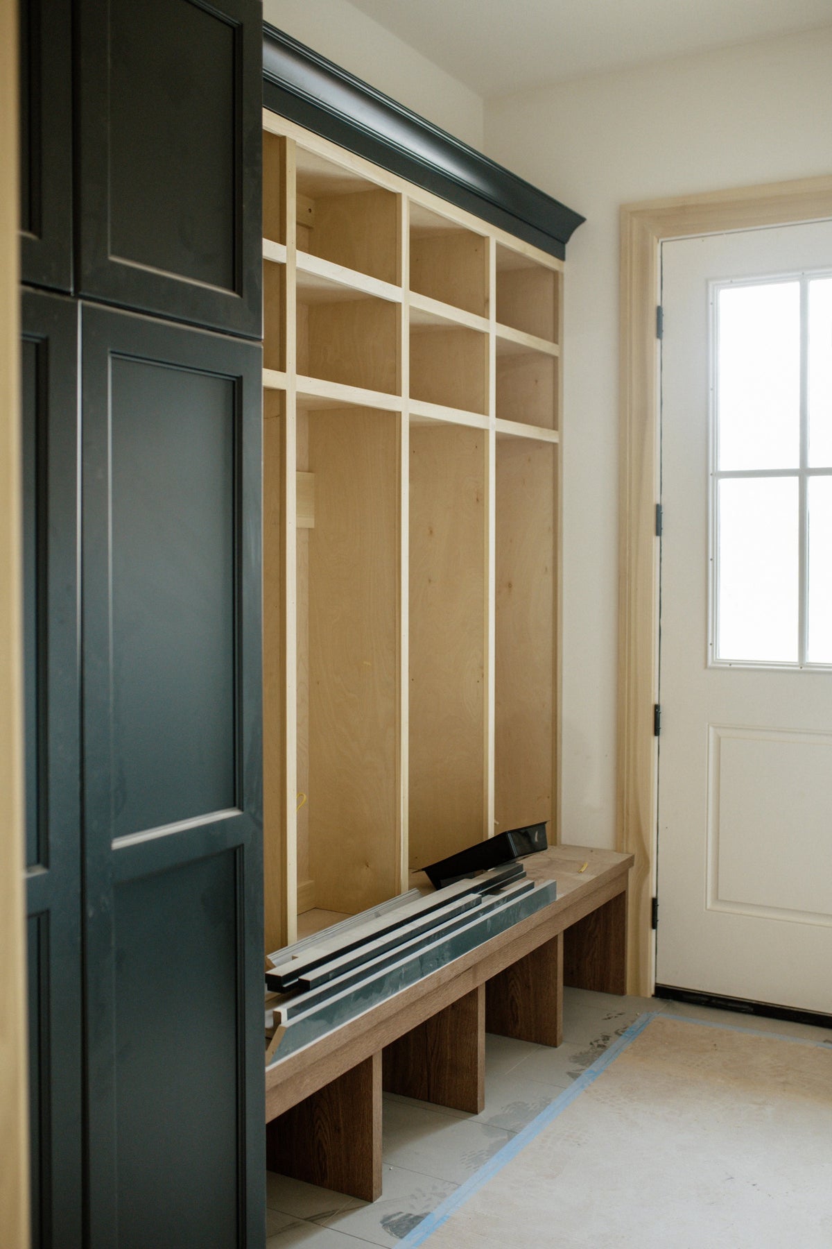 A mudroom under construction in Urbandale with dark green lockers going in beside a white oak bench.