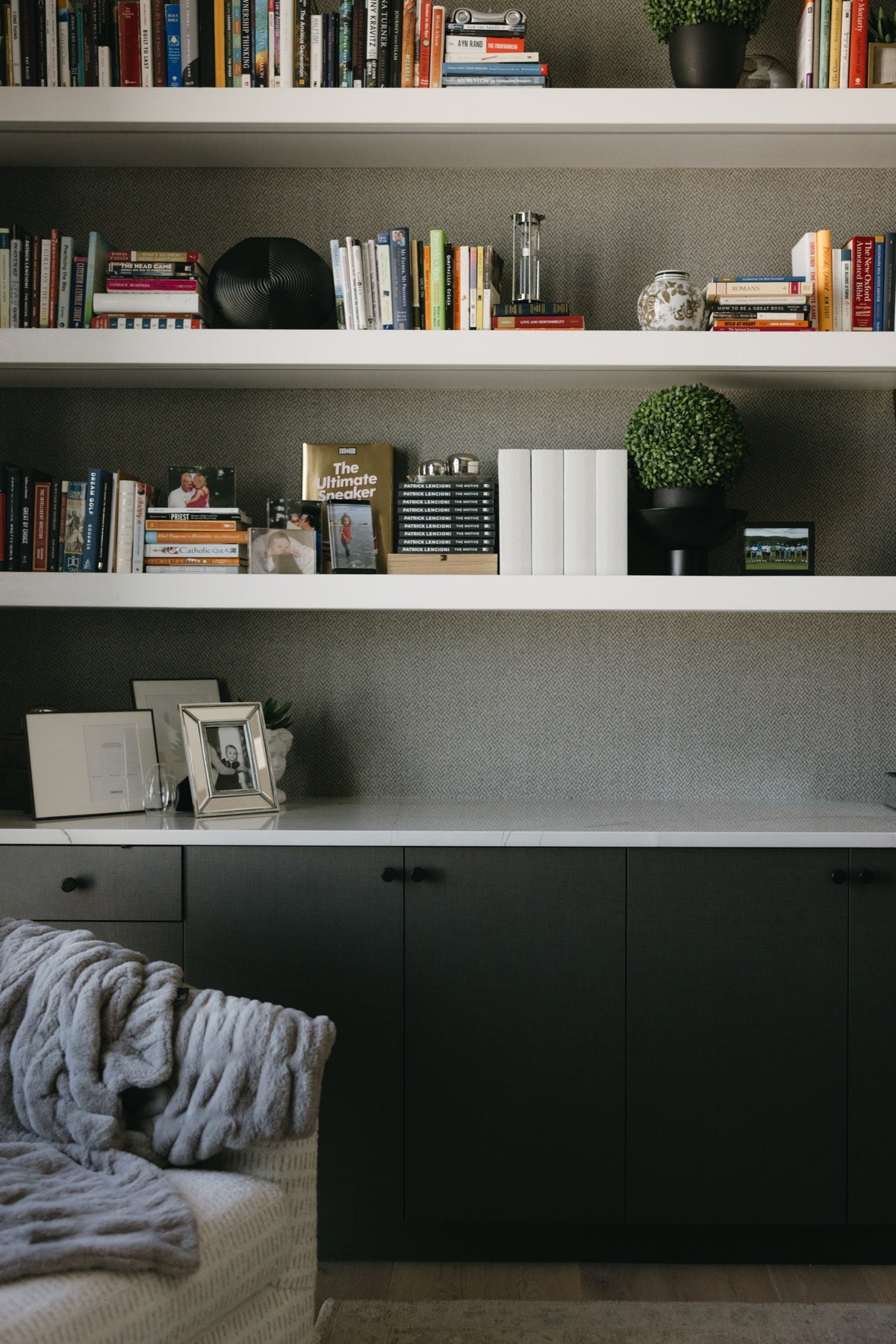 A home office in West Des Moines with white floating bookshelves over dark green cabinets and textured gray wallpaper.