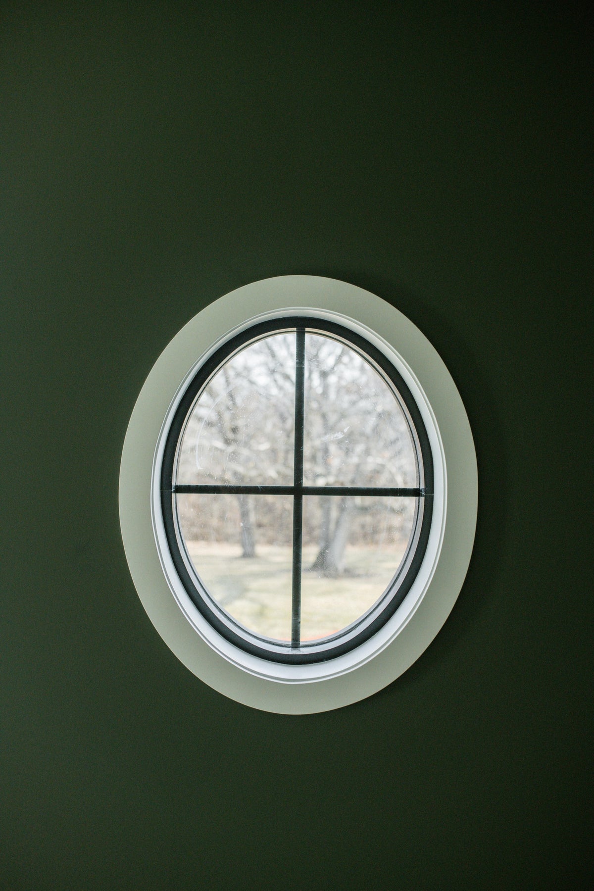 An oval window with black grilles set into a dark green painted wall in a house under construction in Urbandale.