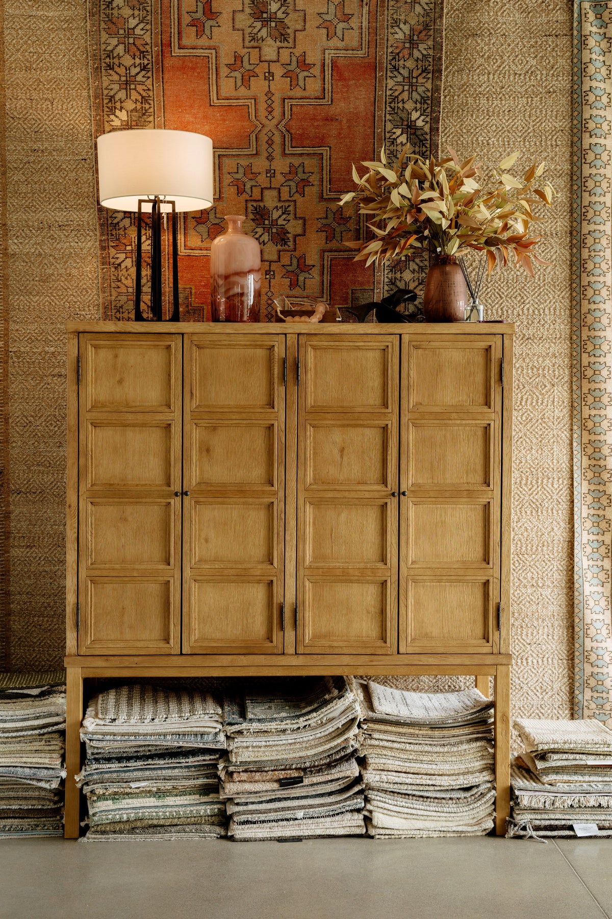 A showroom in Waukee with a paneled white oak cabinet standing over stacks of folded wool and jute rugs.