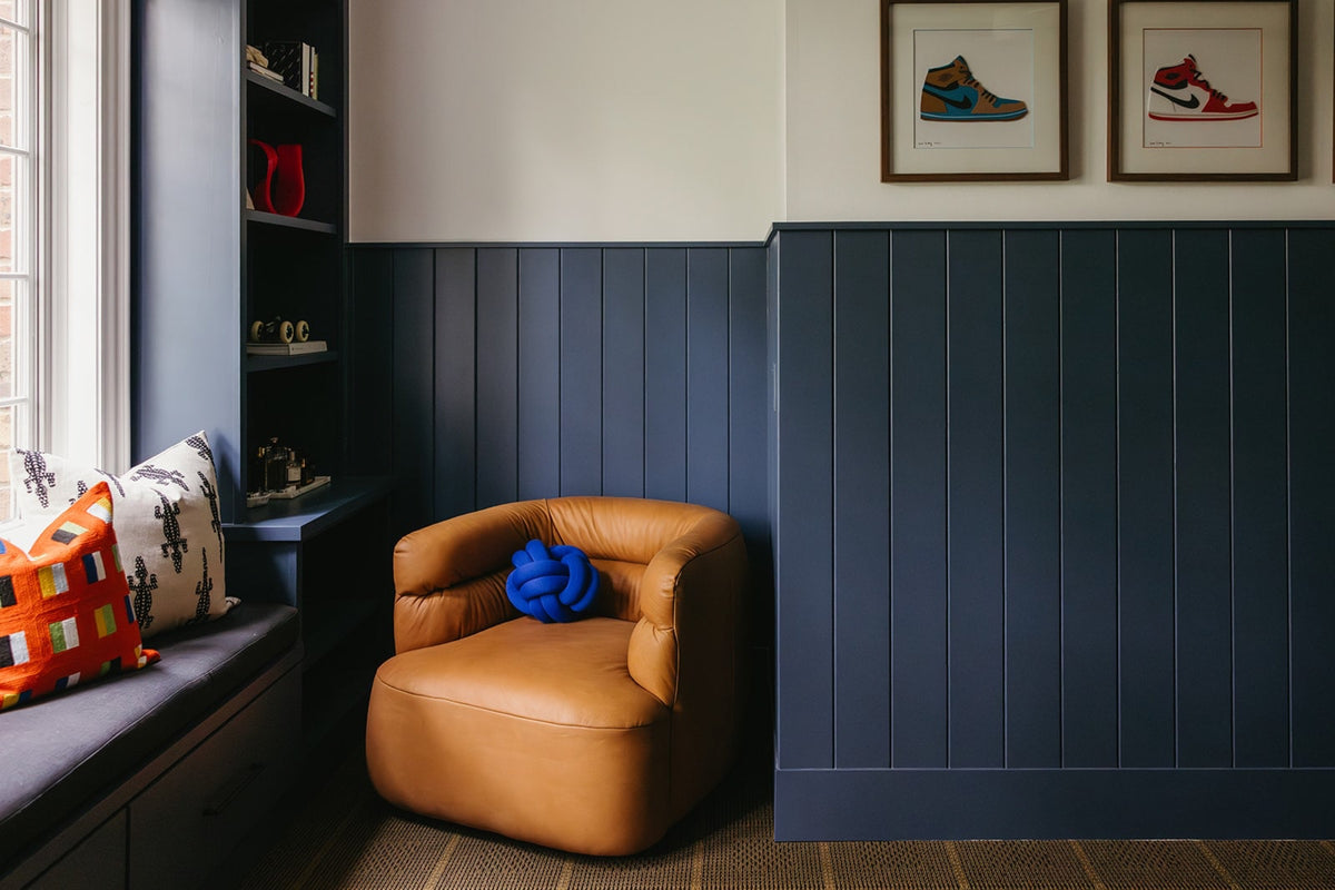 A sitting room in Clive with a tan leather swivel chair against navy vertical paneling.