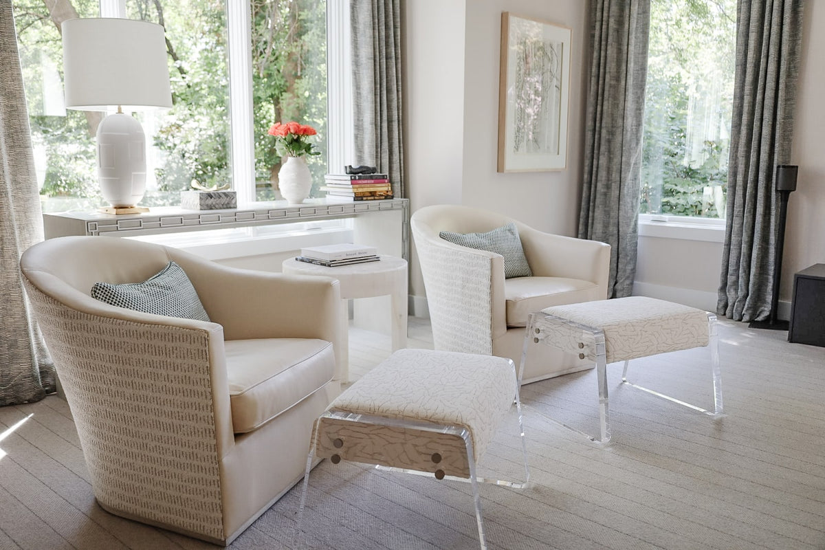 A cream living room in Clive with textured barrel chairs beside an acrylic legged upholstered bench.
