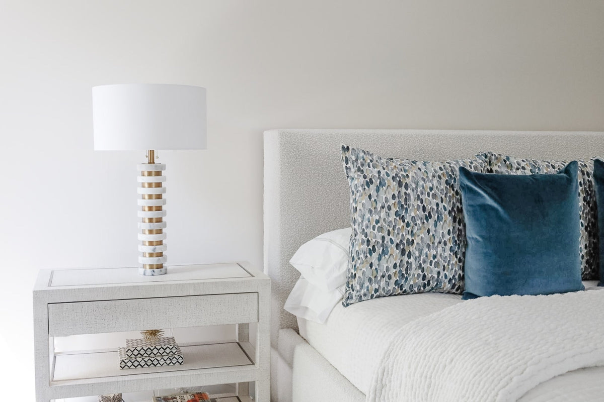 A white bedroom in Clive with a stacked marble and brass lamp on a linen wrapped nightstand.
