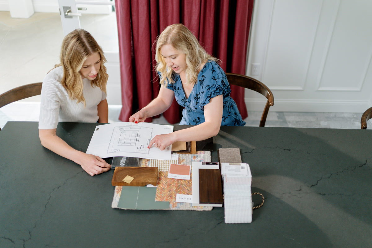 A design consultation in Waukee with a designer pointing at a floor plan over walnut and green samples on a dark counter.