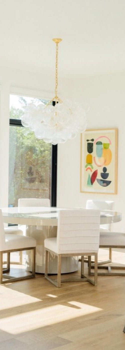 A white dining room with a round table, white chairs and a glass globe chandelier