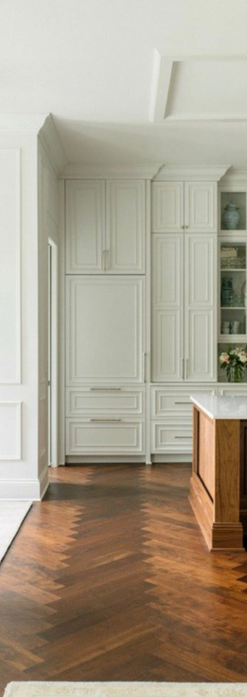 A hallway of painted built-in cabinets over a herringbone wood floor