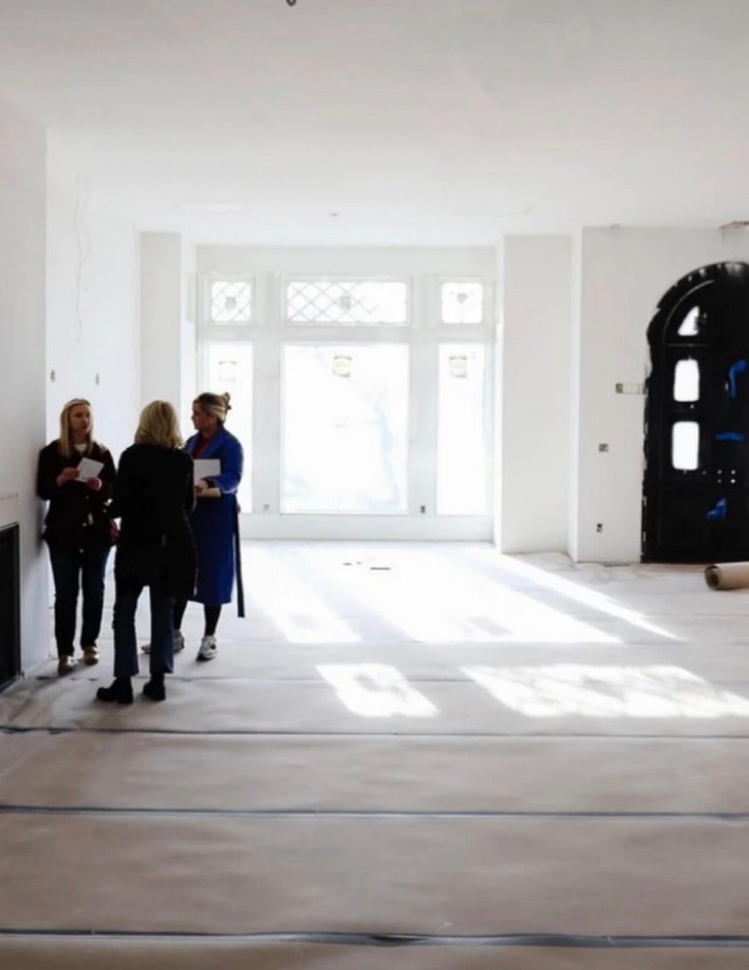 Three people walking an unfinished room with tall leaded windows