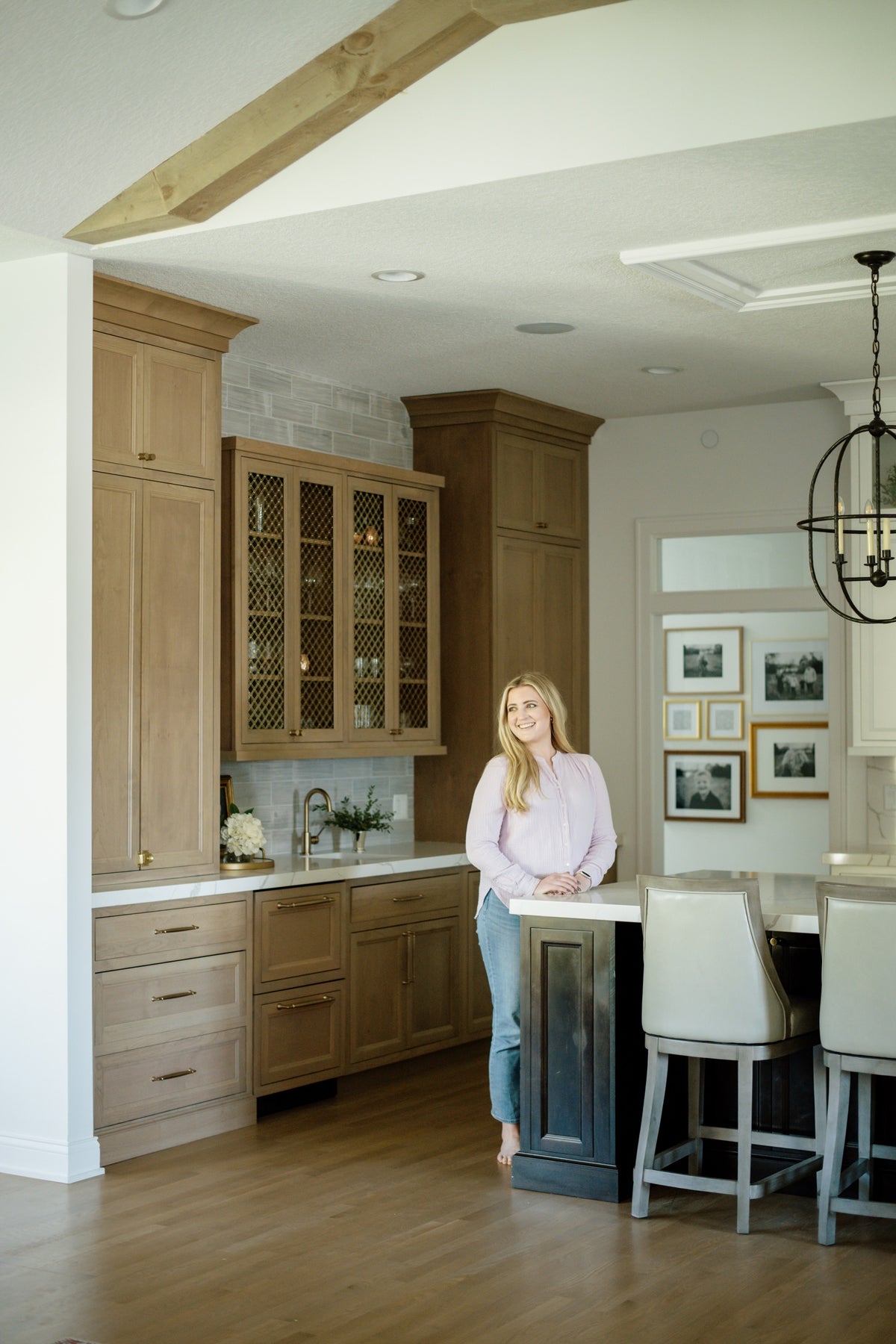 A designer leans on the island in a Johnston kitchen with light oak cabinets and brass hardware.