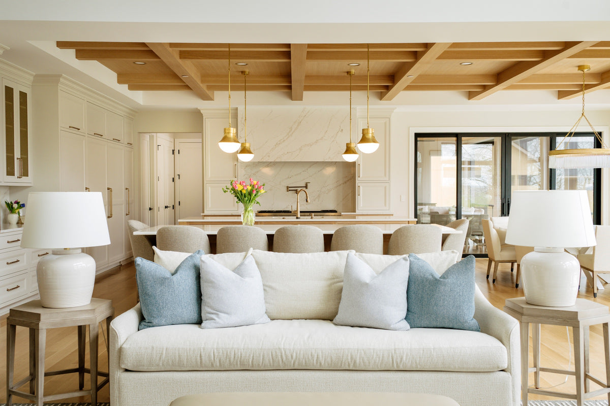 An open living room in West Des Moines with a white oak beamed ceiling above a cream sofa and light oak floors.
