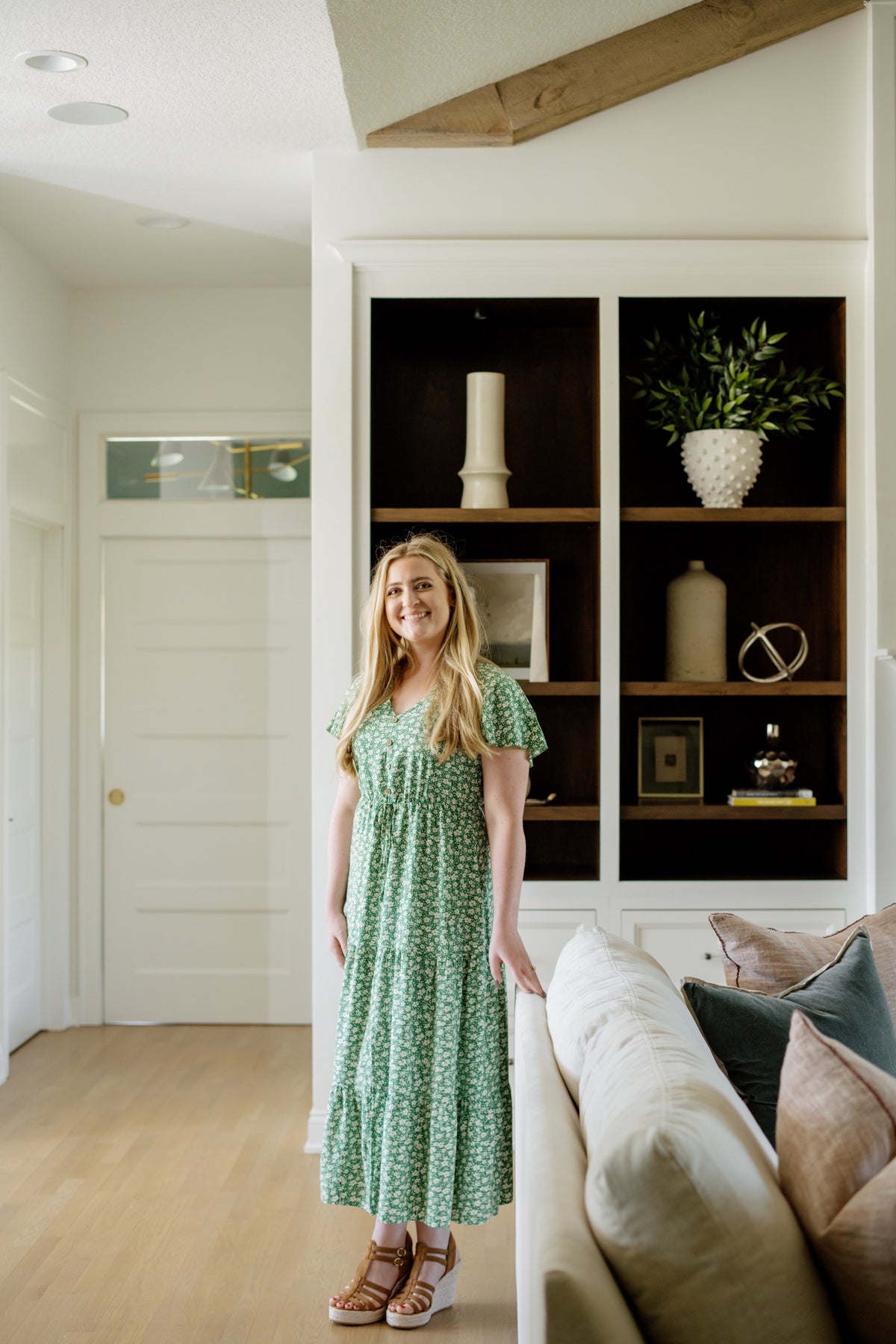 A designer standing in a Johnston living room with white built-ins and dark stained wood shelves behind her.