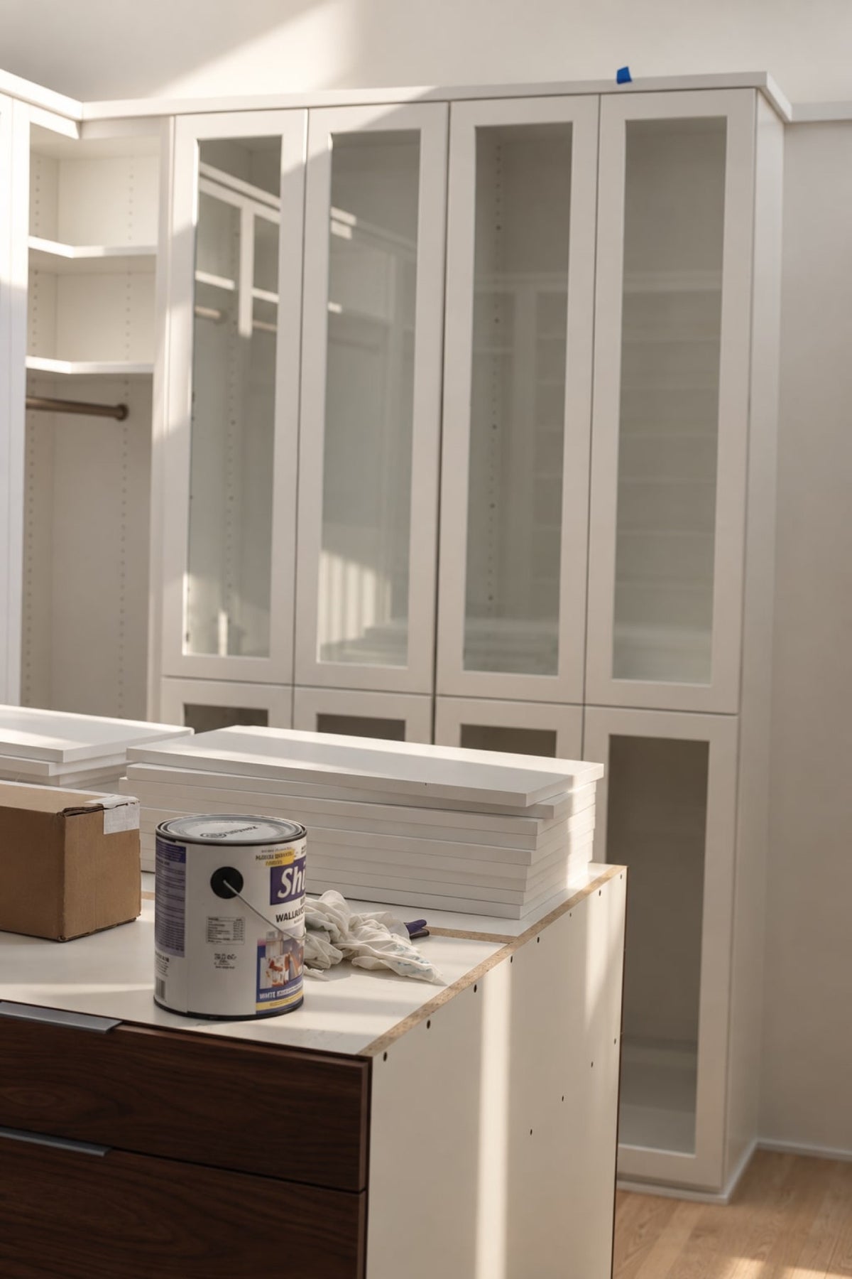 A pantry going in during construction in Des Moines, with white glass-front cabinets along the back wall and shelf boards stacked on a half-built island.