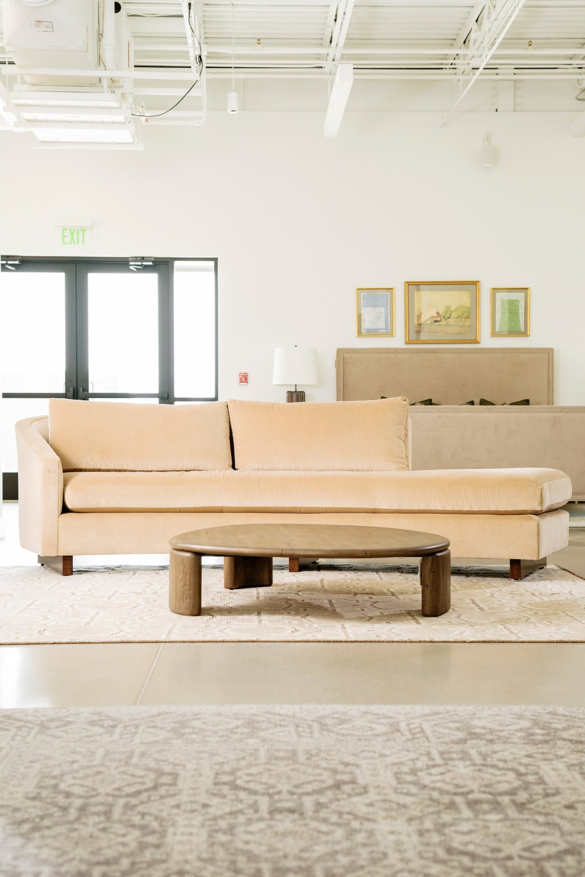 A showroom in Waukee with a cream velvet chaise sofa behind a round oak coffee table on a woven rug.