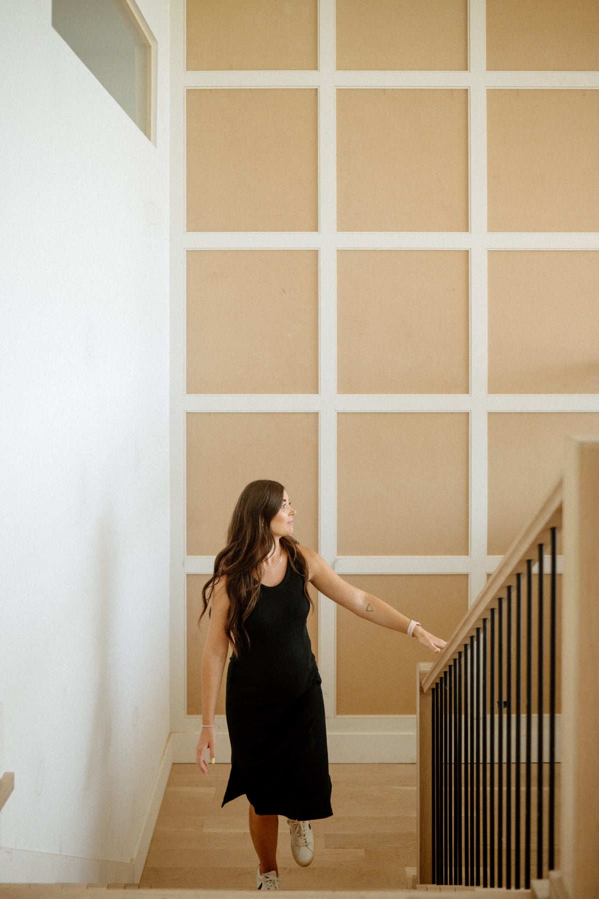 A designer at the railing in a West Des Moines stairwell with a tall grid-panel accent wall in warm tan.