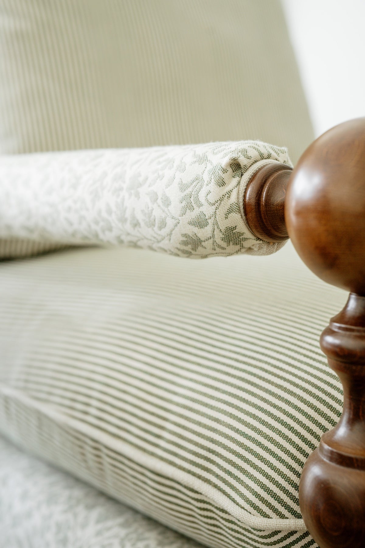 An upholstered chair in Waukee with a green leaf print rolled arm against a green striped seat.